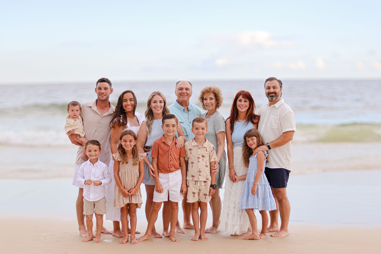 Family group in coordinated beige and blue outfits poses together on a sunset beach.