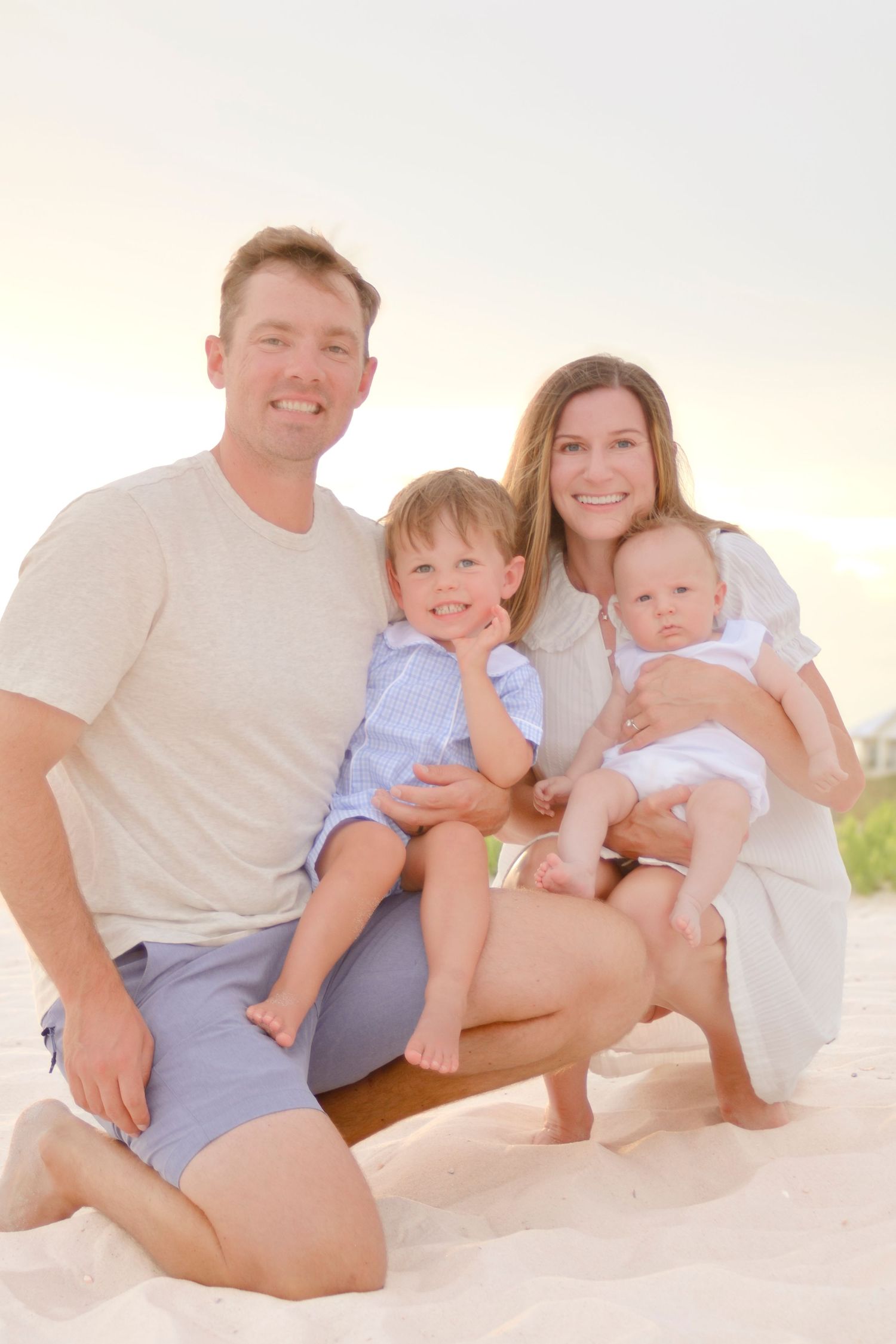 Family sitting together on sandy beach during golden sunset in casual summer attire.