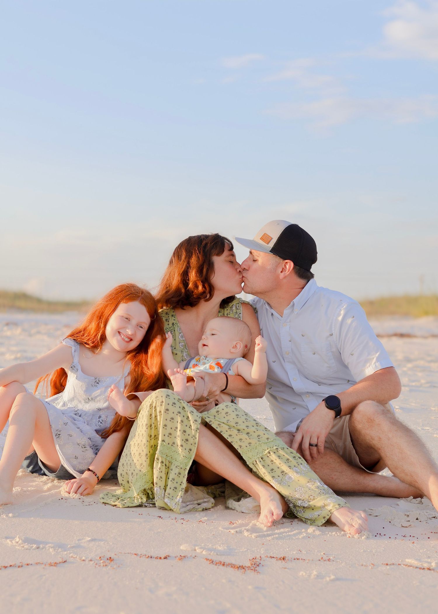 A loving family sitting together and laughing on a sunny beach at sunset.