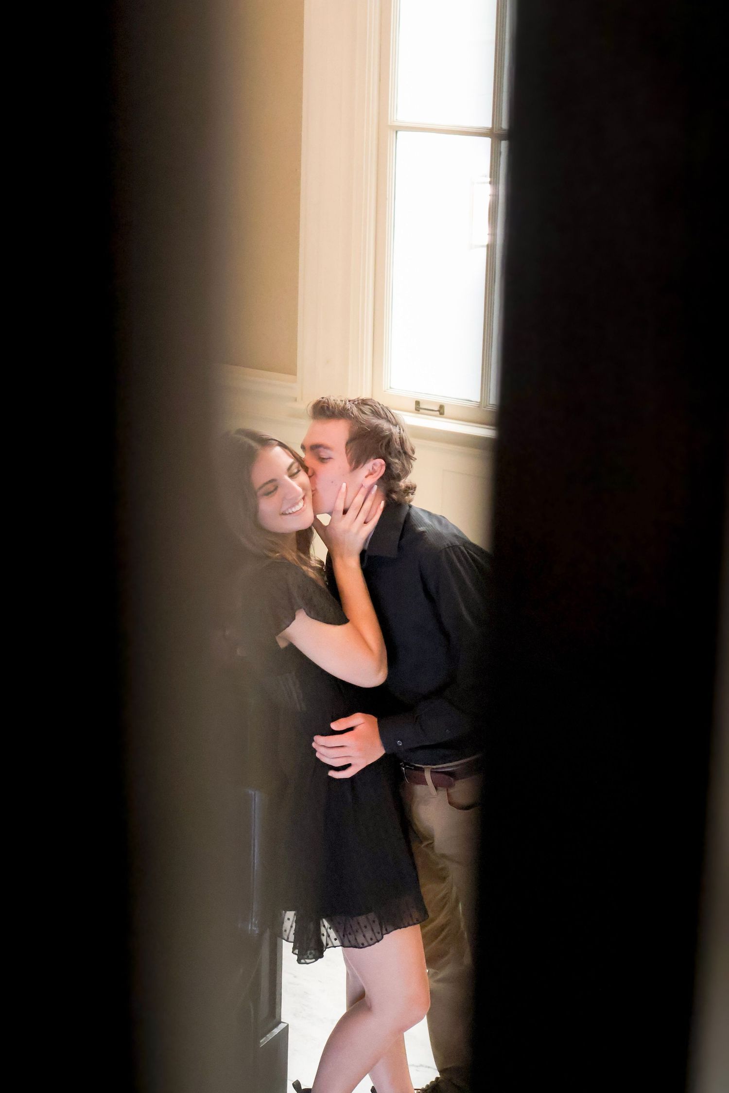 A couple embracing in dramatic light by a window, captured in a series of three black and white photographs.