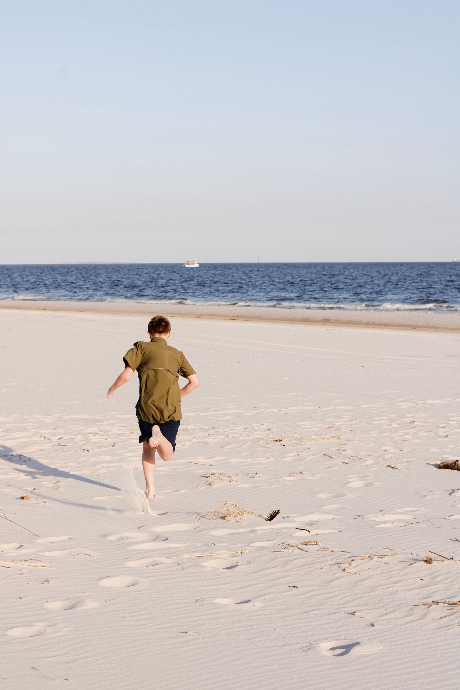 Person in green shirt running along pristine white sandy beach with blue ocean horizon in the background.