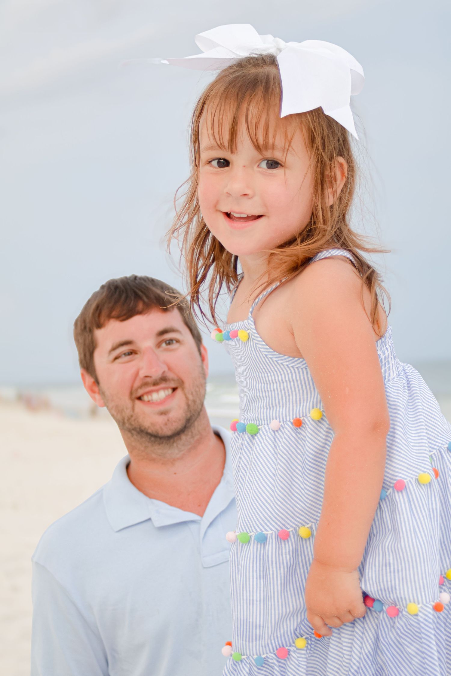 Sweet portrait on a bright beach of a small child in a white striped dress with a bow and a smiling adult.
