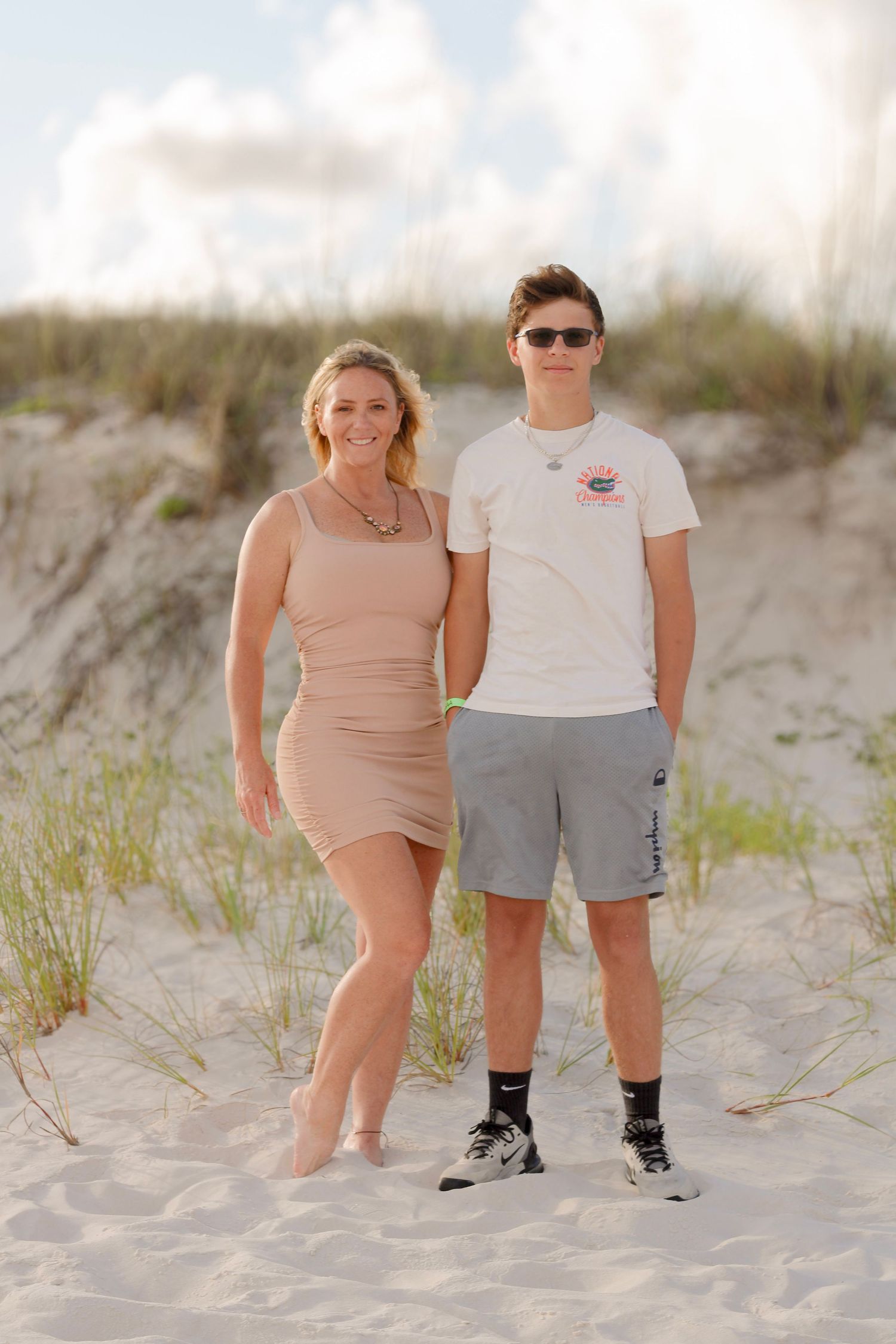 Casual summer portrait featuring two people standing together on sandy beach dunes during golden hour.