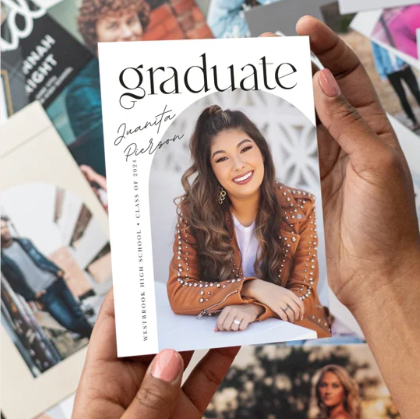 Hands holding out a white business card against a background of printed photographs and marketing materials.