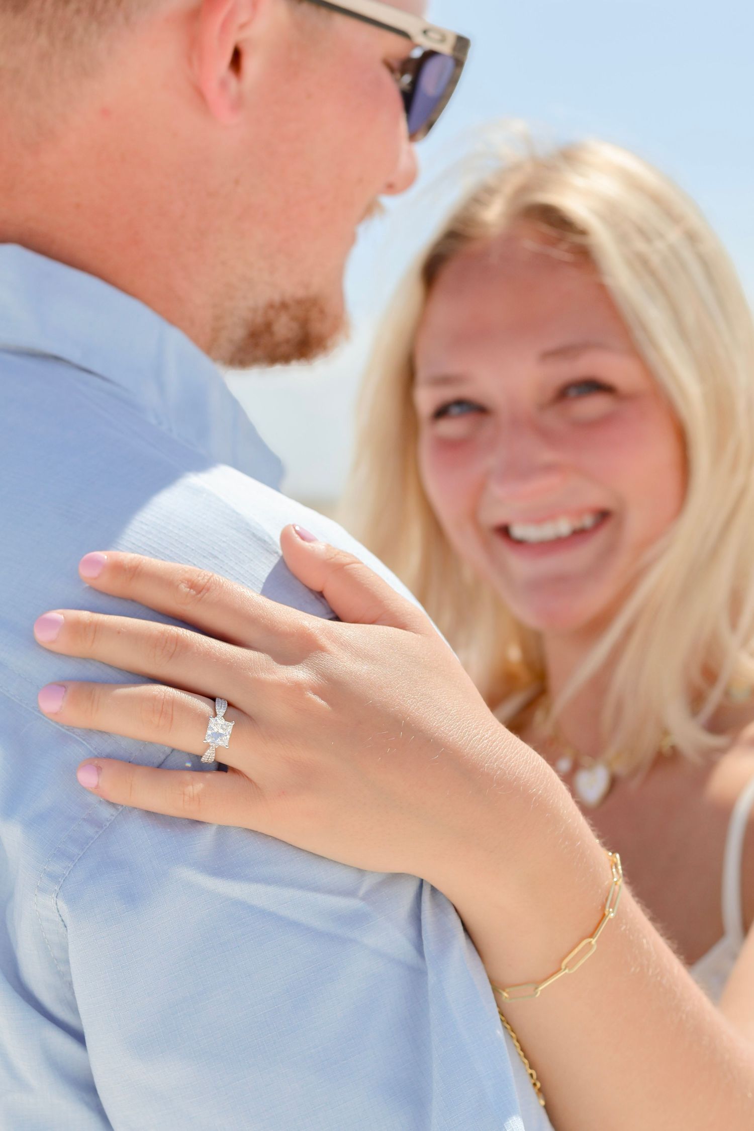 A close-up shot of a newly engaged couple showing off the diamond engagement ring while sharing a joyful moment outdoors.