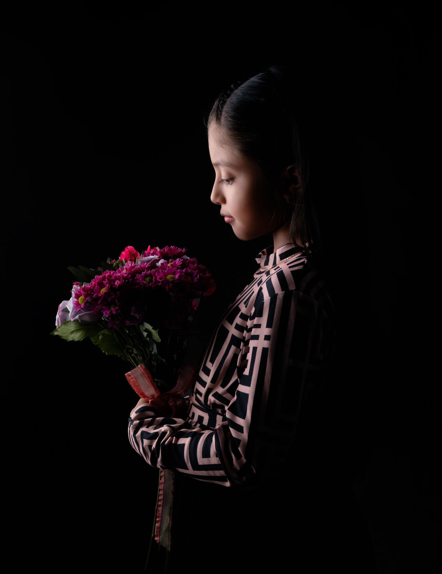 Dramatic low-key portrait with pink flowers against black background.