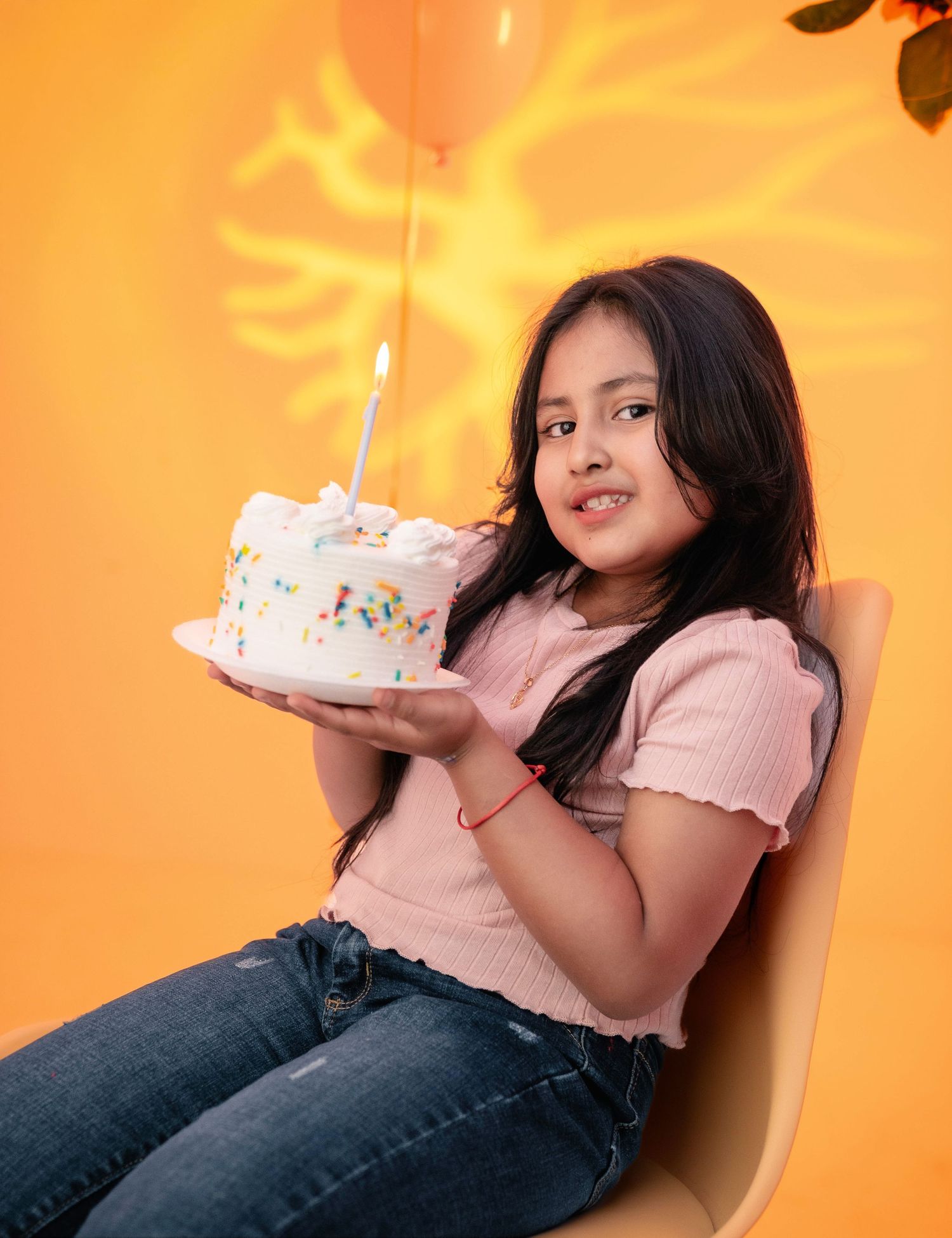 Person in pink shirt and jeans reclining with birthday cake in warm orange lighting.