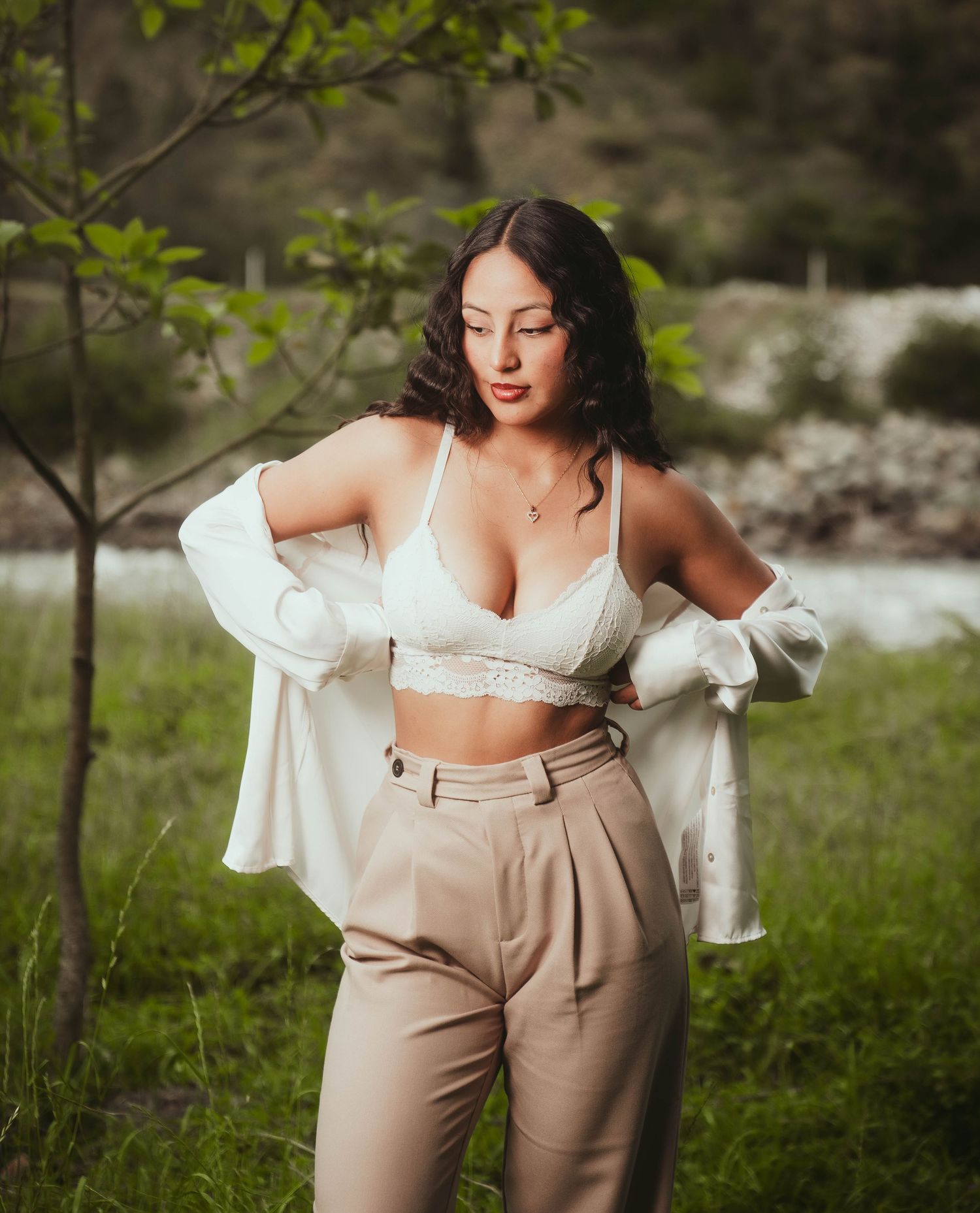 Fashion portrait of a woman in white crop top and beige pants posing in a spring garden setting.