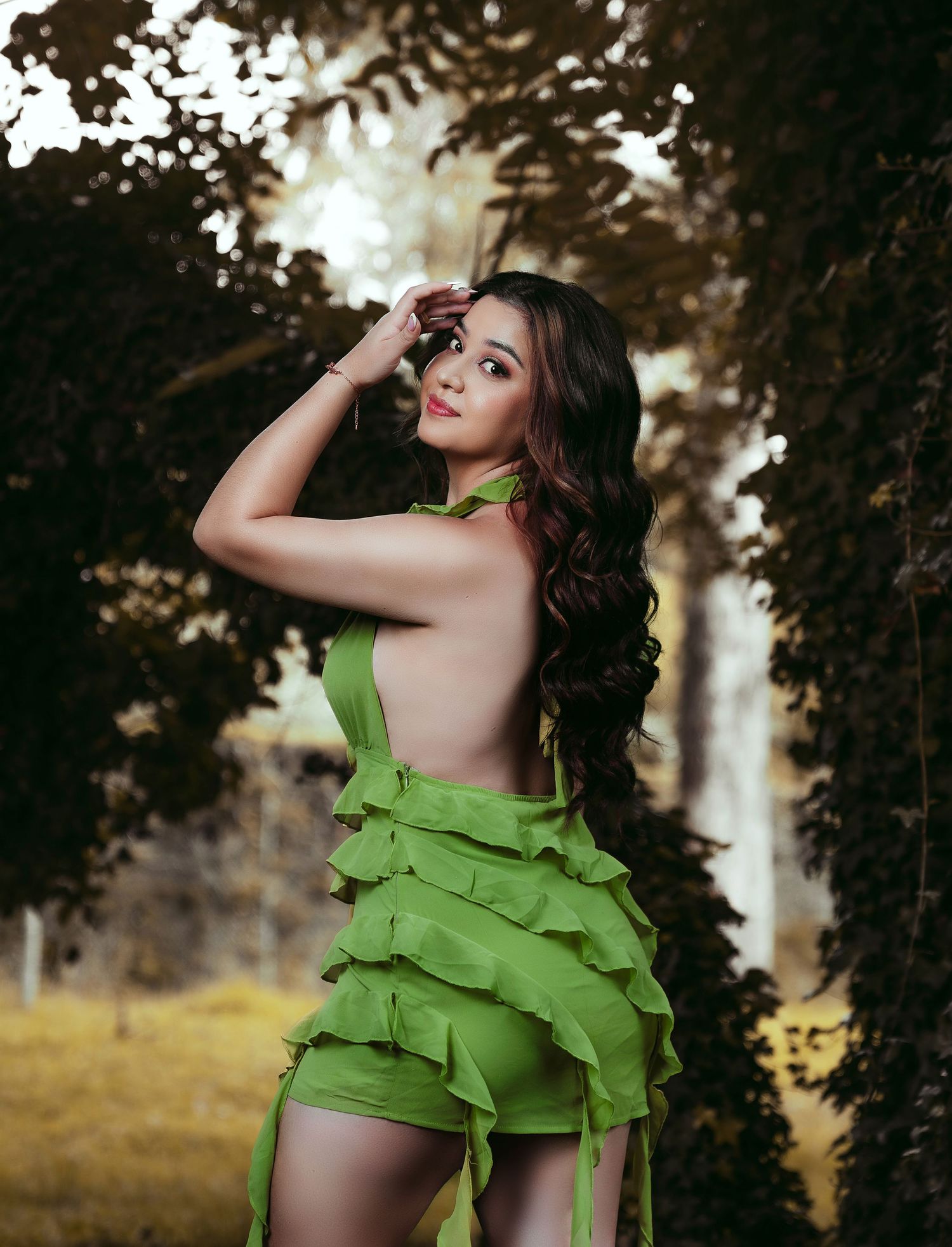 Artistic portrait in a layered green dress against dreamy forest backdrop.