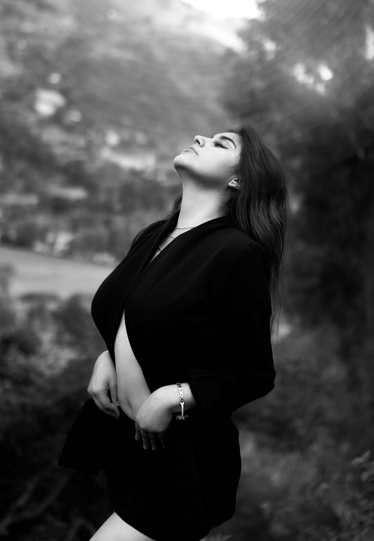 Dramatic black and white portrait of woman in dark clothing looking upward outdoors.