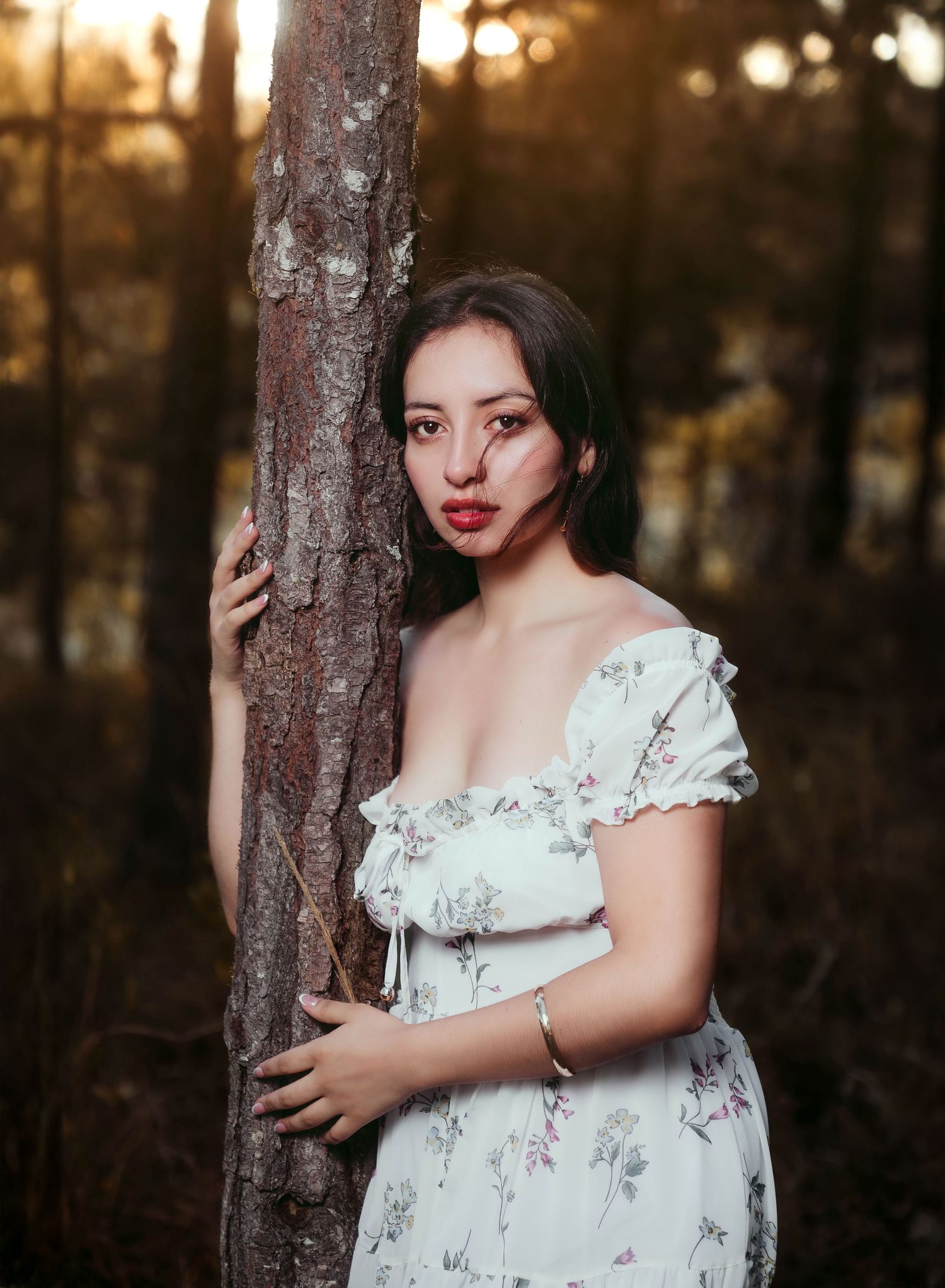 Romantic forest photography featuring white floral dress against sunset-lit trees.