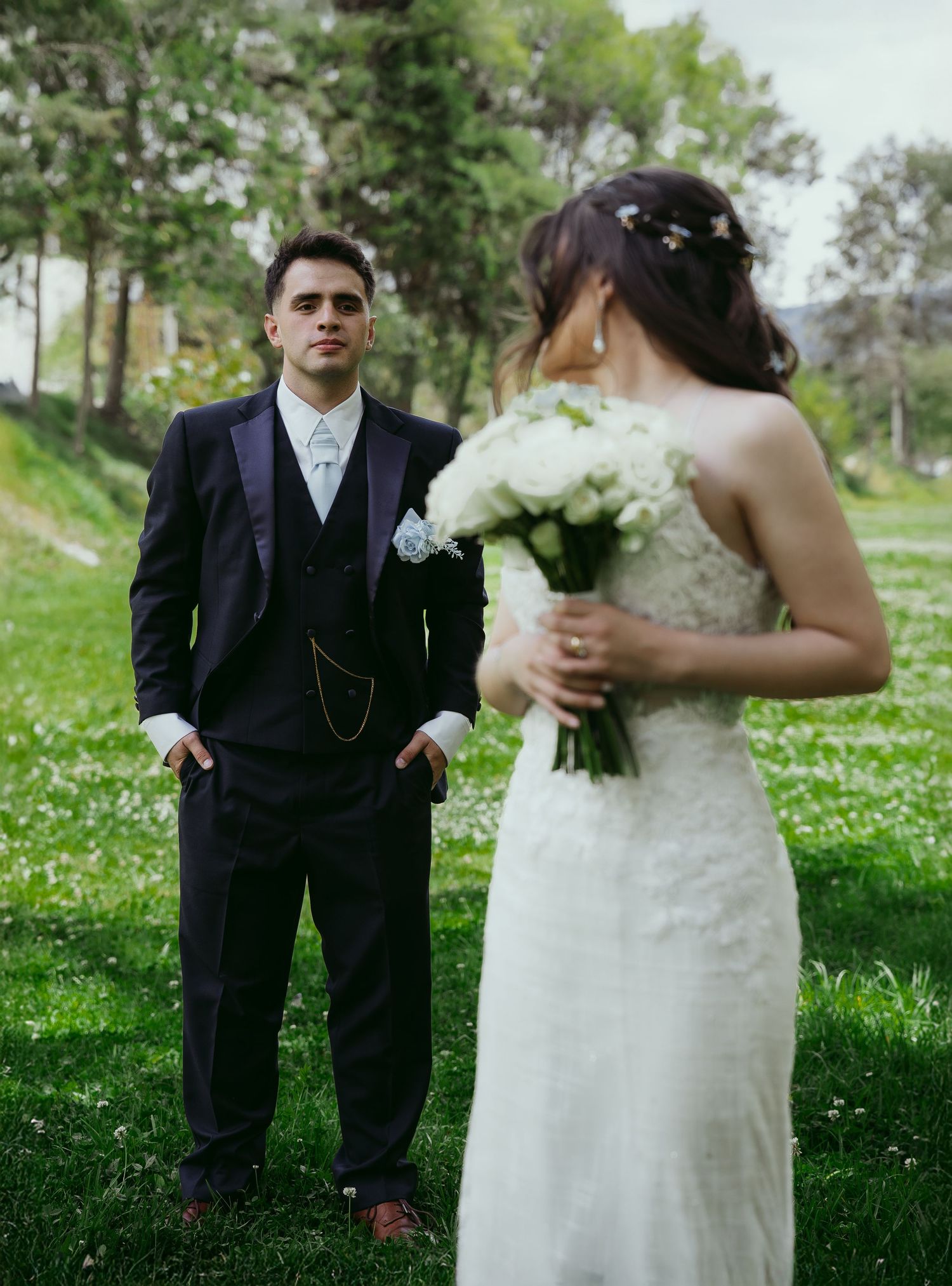 Wedding couple stands in a lush green garden setting during their outdoor spring ceremony.