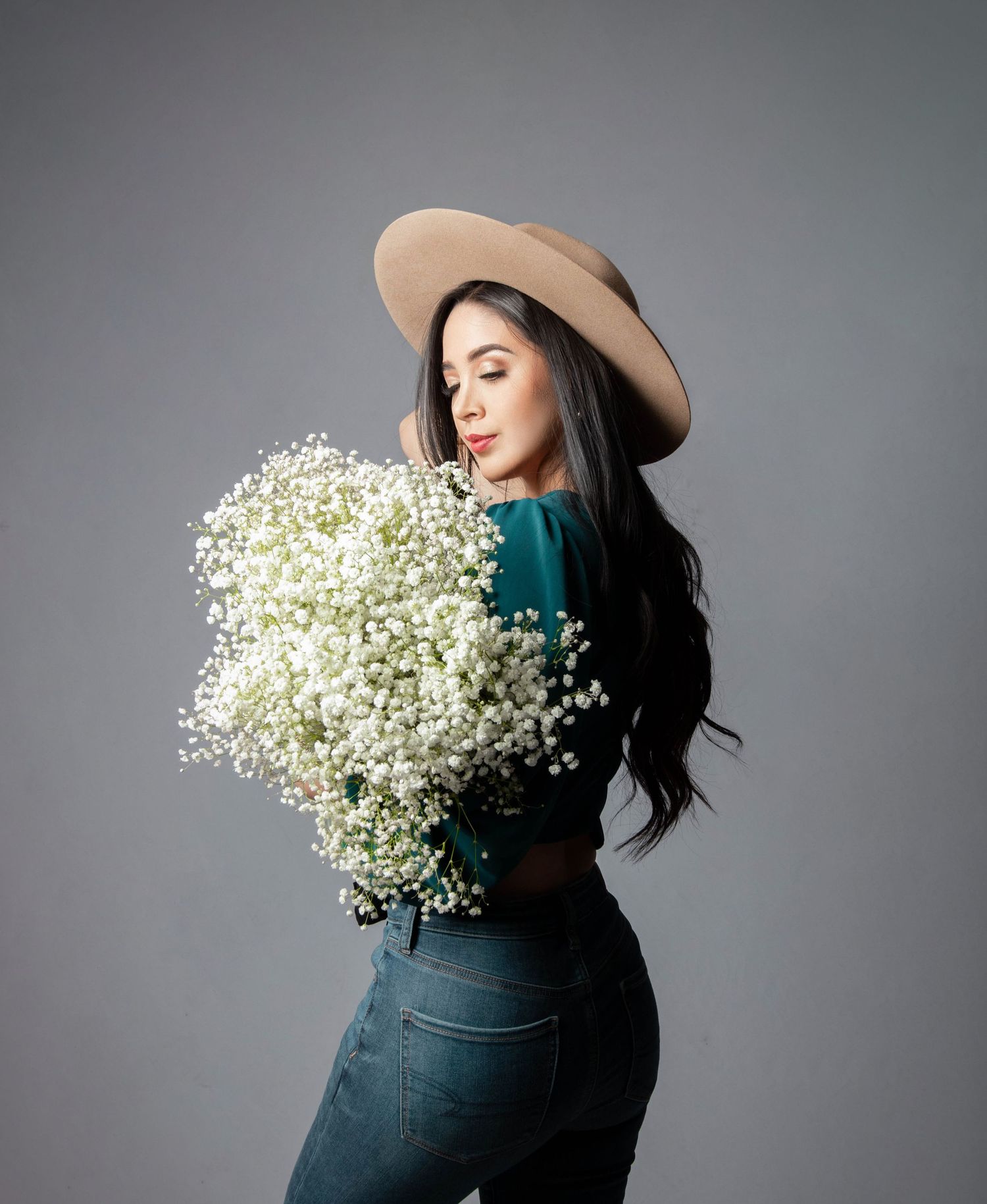 Woman in hat holds large bouquet of baby's breath flowers against grey backdrop.