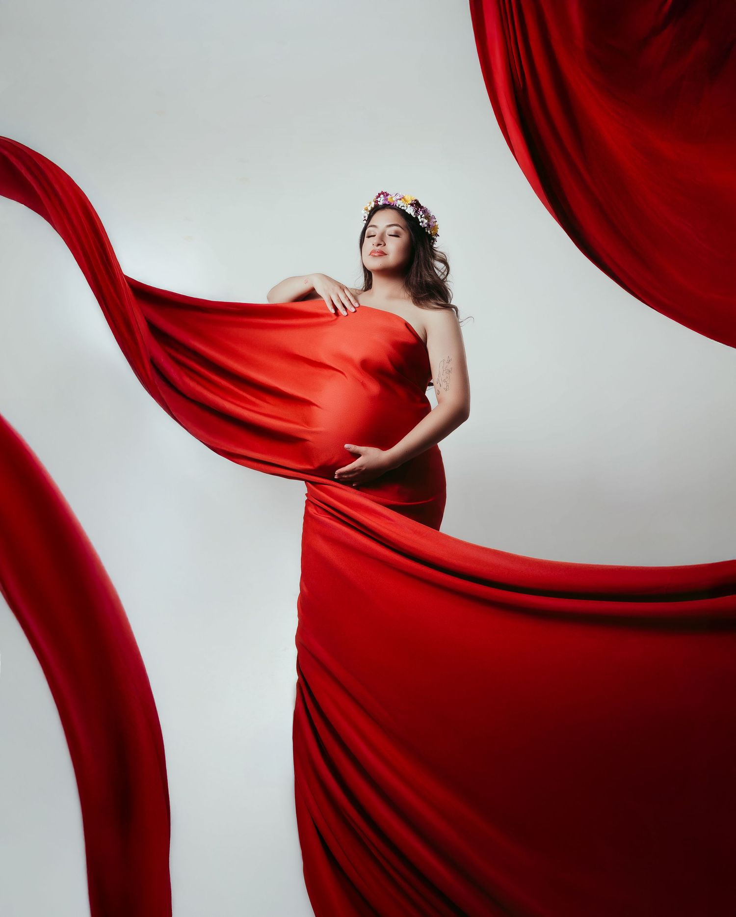 Dramatic portrait with flowing red fabric against white background.