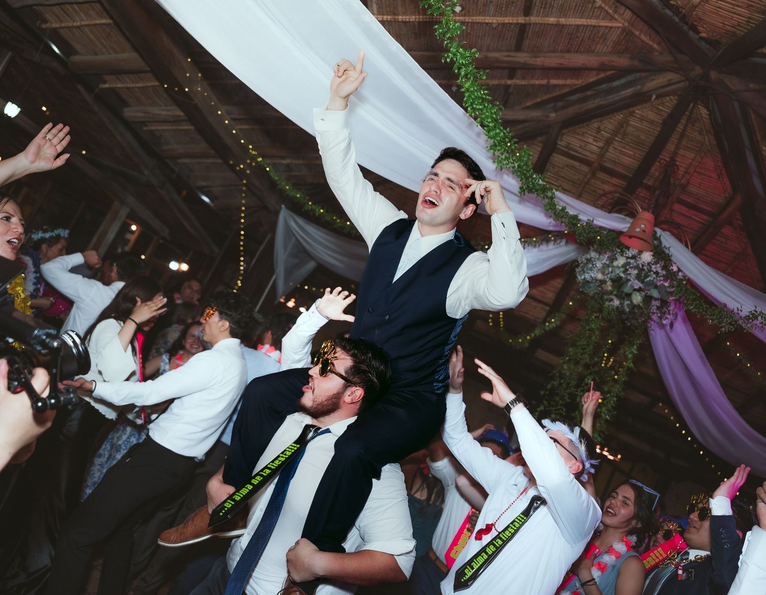 Dancers move energetically on a dimly lit dance floor during a wedding reception celebration.