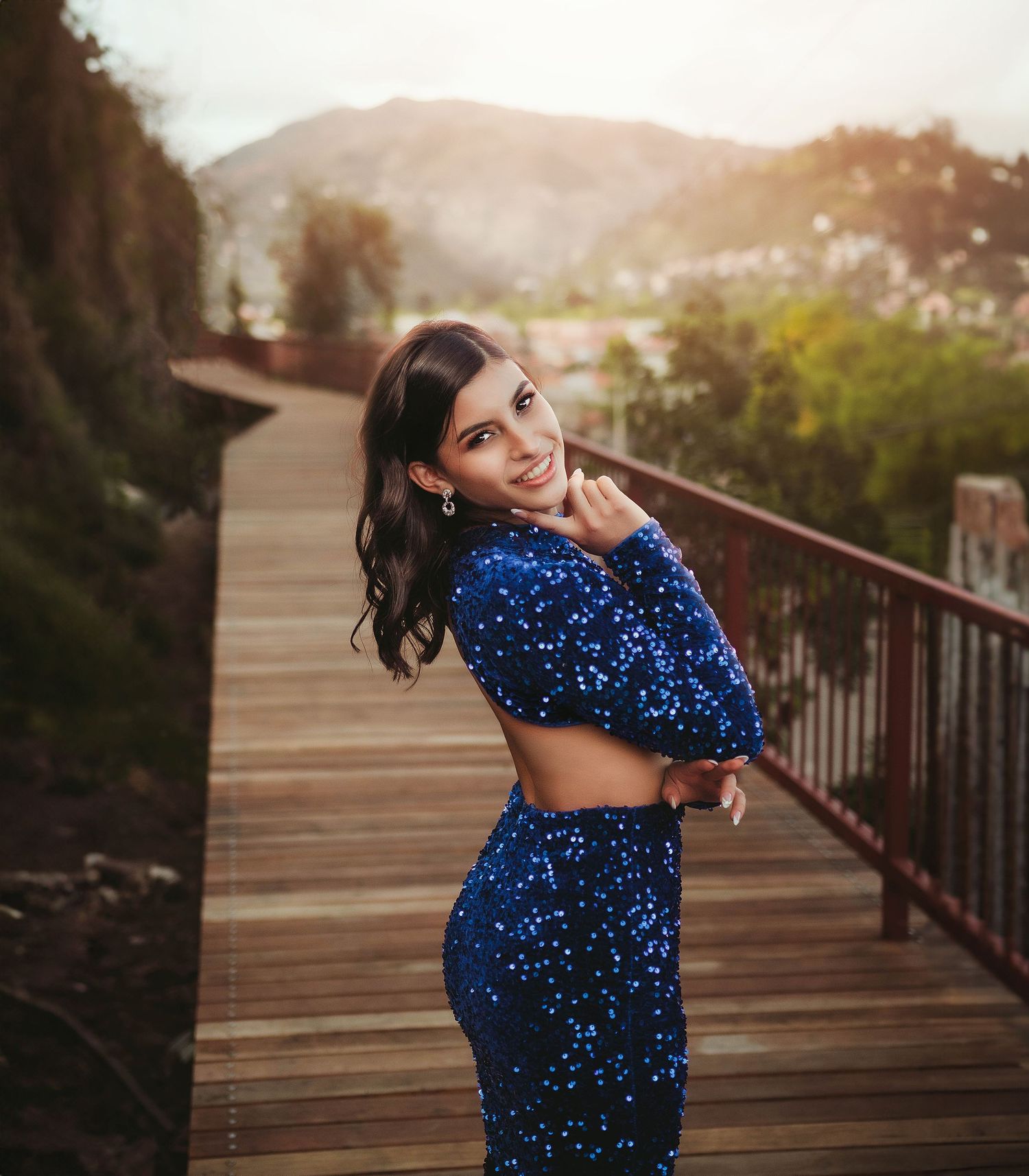 Person in sparkling blue two-piece outfit poses on wooden bridge at sunset.
