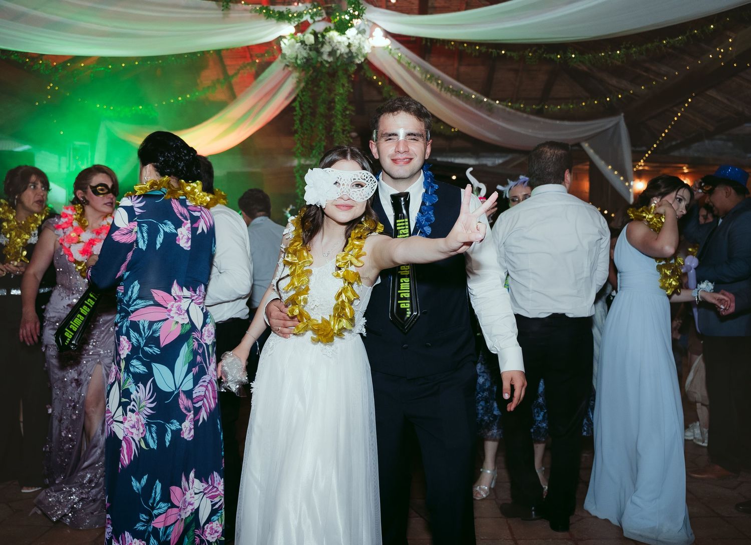 Wedding reception dance floor scene with guests celebrating under draped fabric and twinkle lights in green lighting.