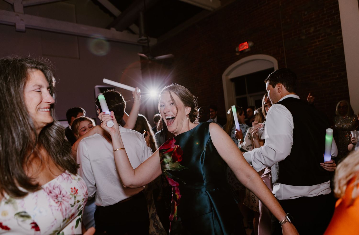 Women laughing and dancing with glow sticks at an elegant wedding reception party.