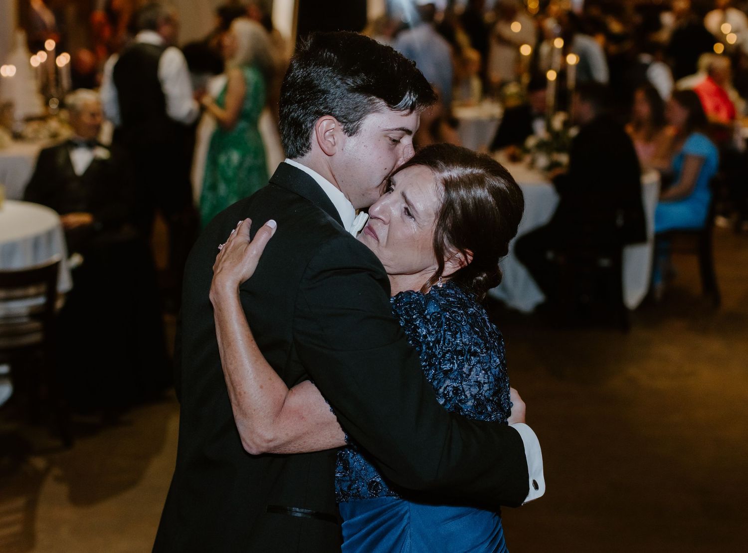 Couple sharing a romantic dance embrace at an elegant wedding reception with guests seated in background.
