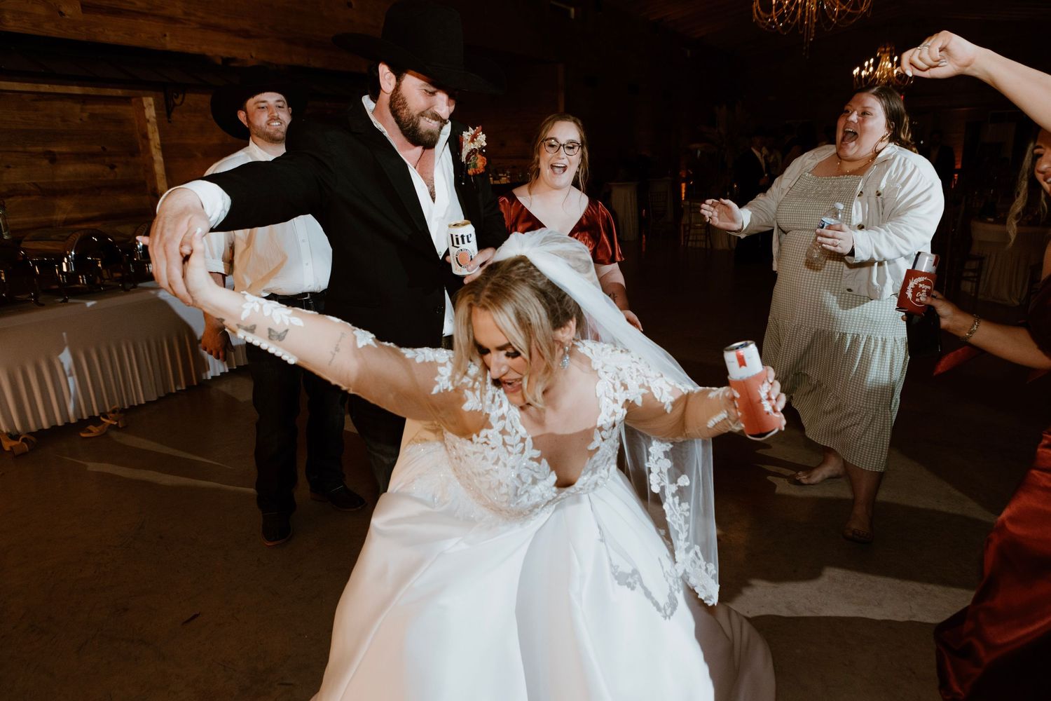 Bride and groom dancing joyfully at wedding reception with guests celebrating in background.