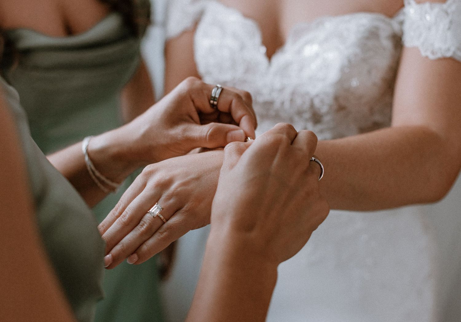 Bride having wedding ring placed on her finger during ceremony, with bridesmaids in sage green dresses assisting.