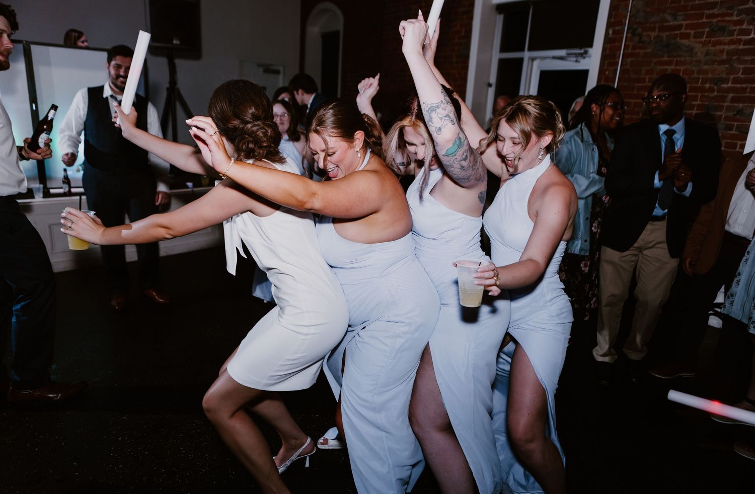 Bridesmaids in light blue dresses dancing and celebrating together on the wedding reception dance floor.