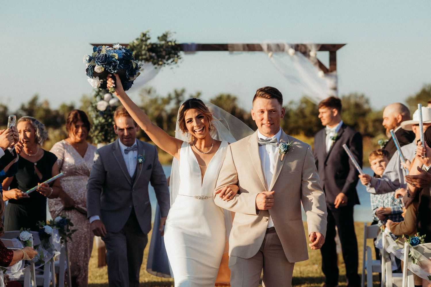 Wedding couple walking down aisle while guests throw flower petals in outdoor ceremony.