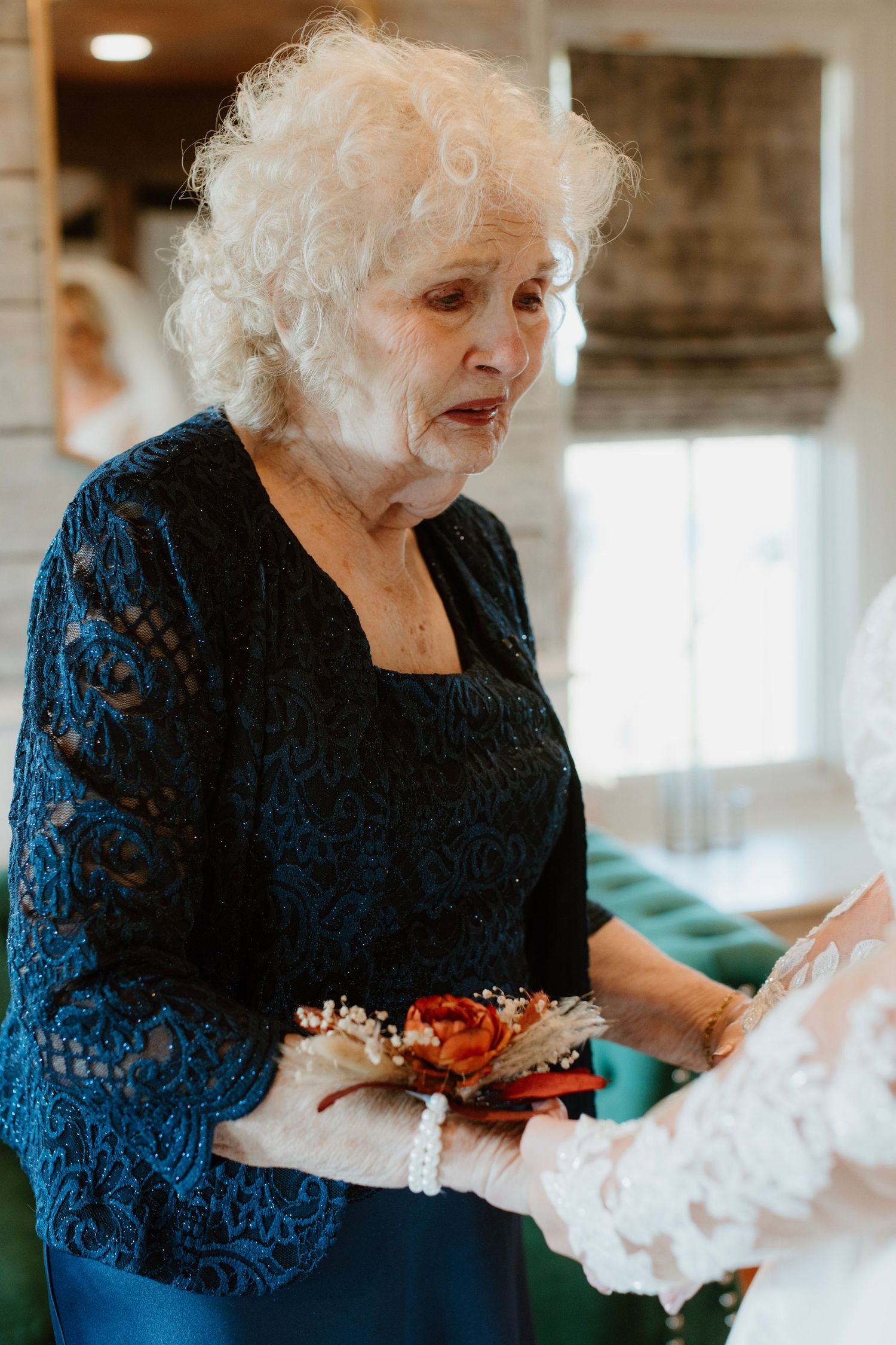 Elderly woman in blue lace top holds floral corsage at wedding ceremony.