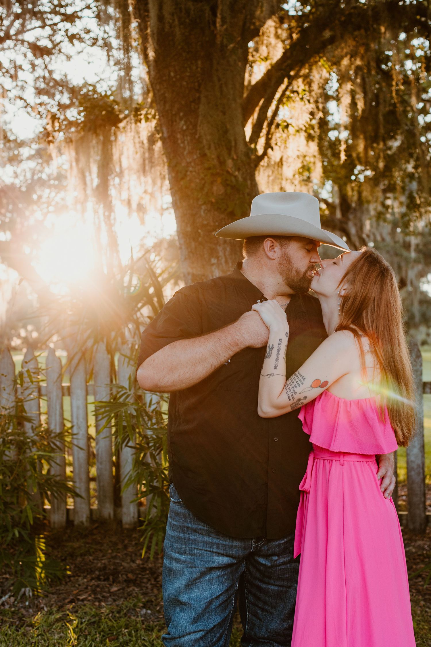 A couple shares a tender moment at sunset with Spanish moss hanging from trees in the background.