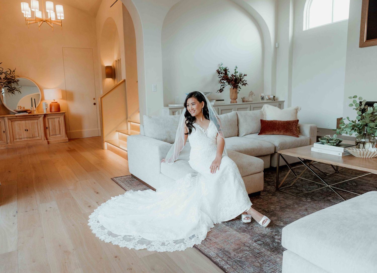 A wedding dress with delicate lace details drapes elegantly across a bright white modern living room with arched details.