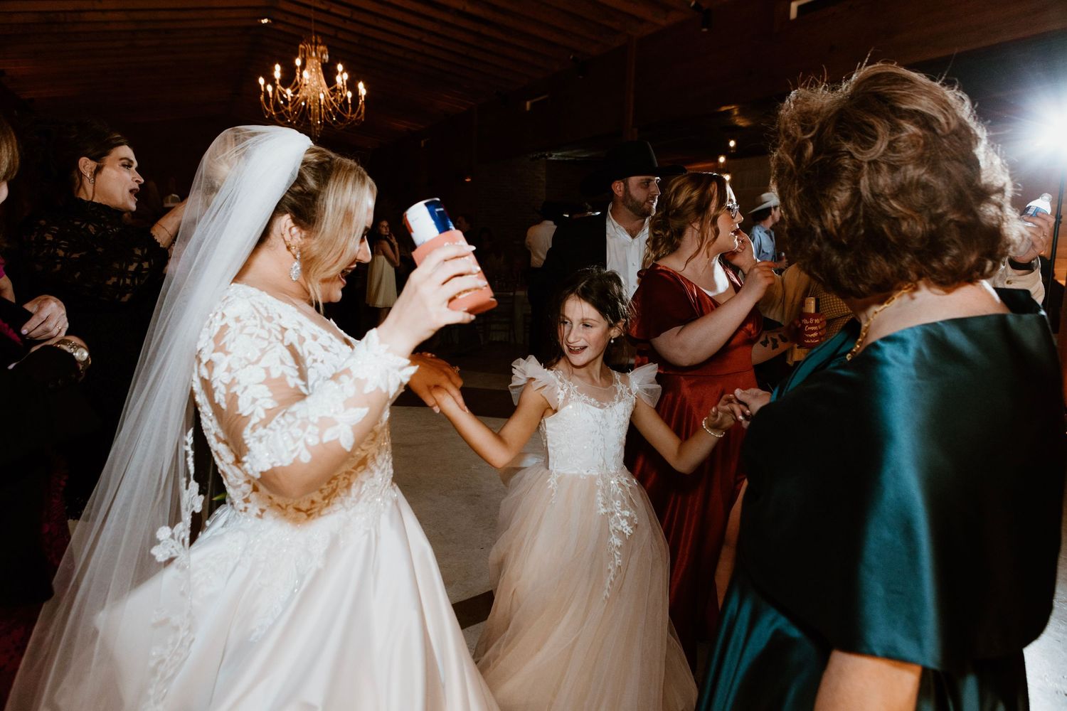 Bride in lace wedding gown dances with flower girl in white dress at elegant wedding reception.