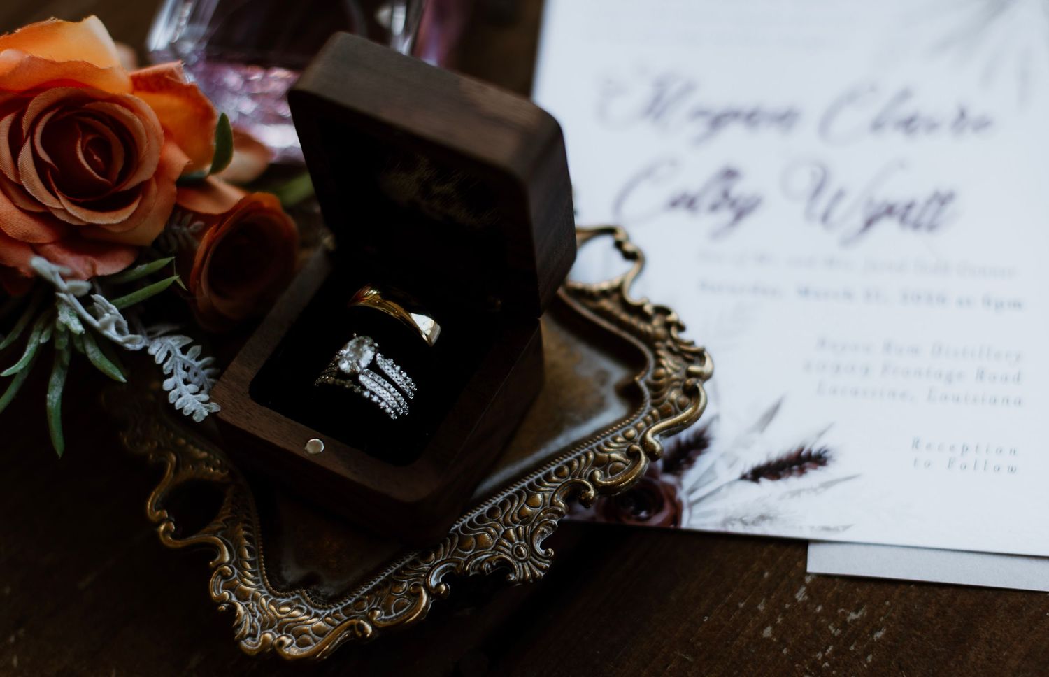 Wedding rings in dark wooden box on ornate tray with roses and invitation for Megan Claire and Cody Wyatt.