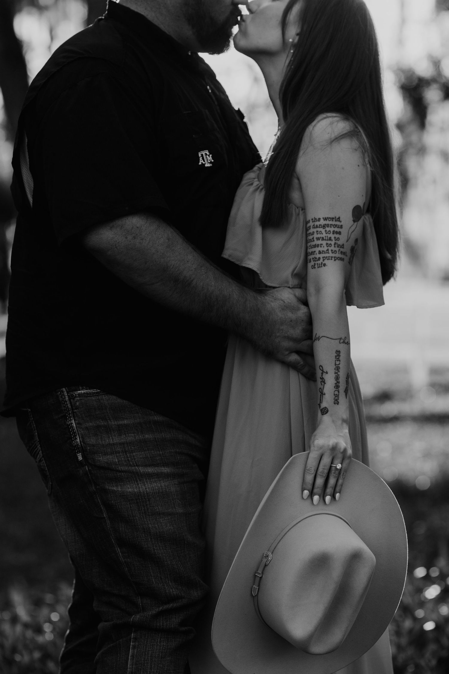 Intimate black and white engagement photo showing couple embracing in casual outfits during outdoor photoshoot.