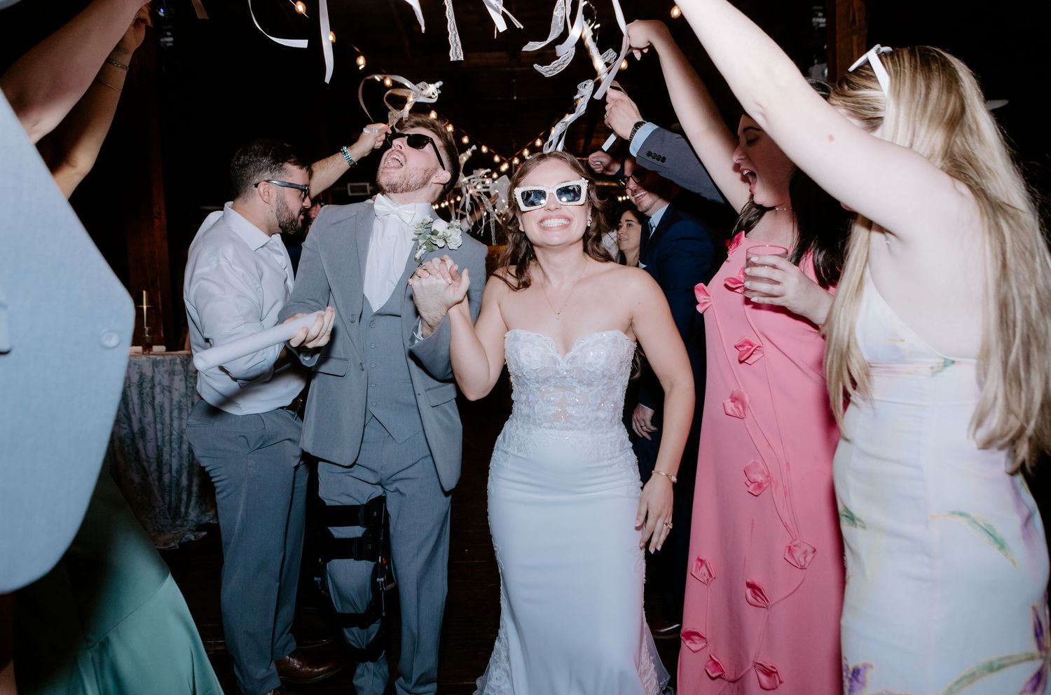 Bride in strapless gown and groom walking through cheering guests with streamers at wedding sendoff.