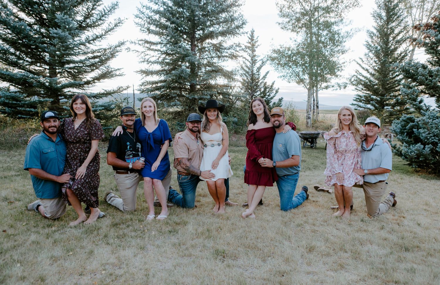 Group of ten people posing outdoors near evergreen trees in a mountain setting for a casual family photo.