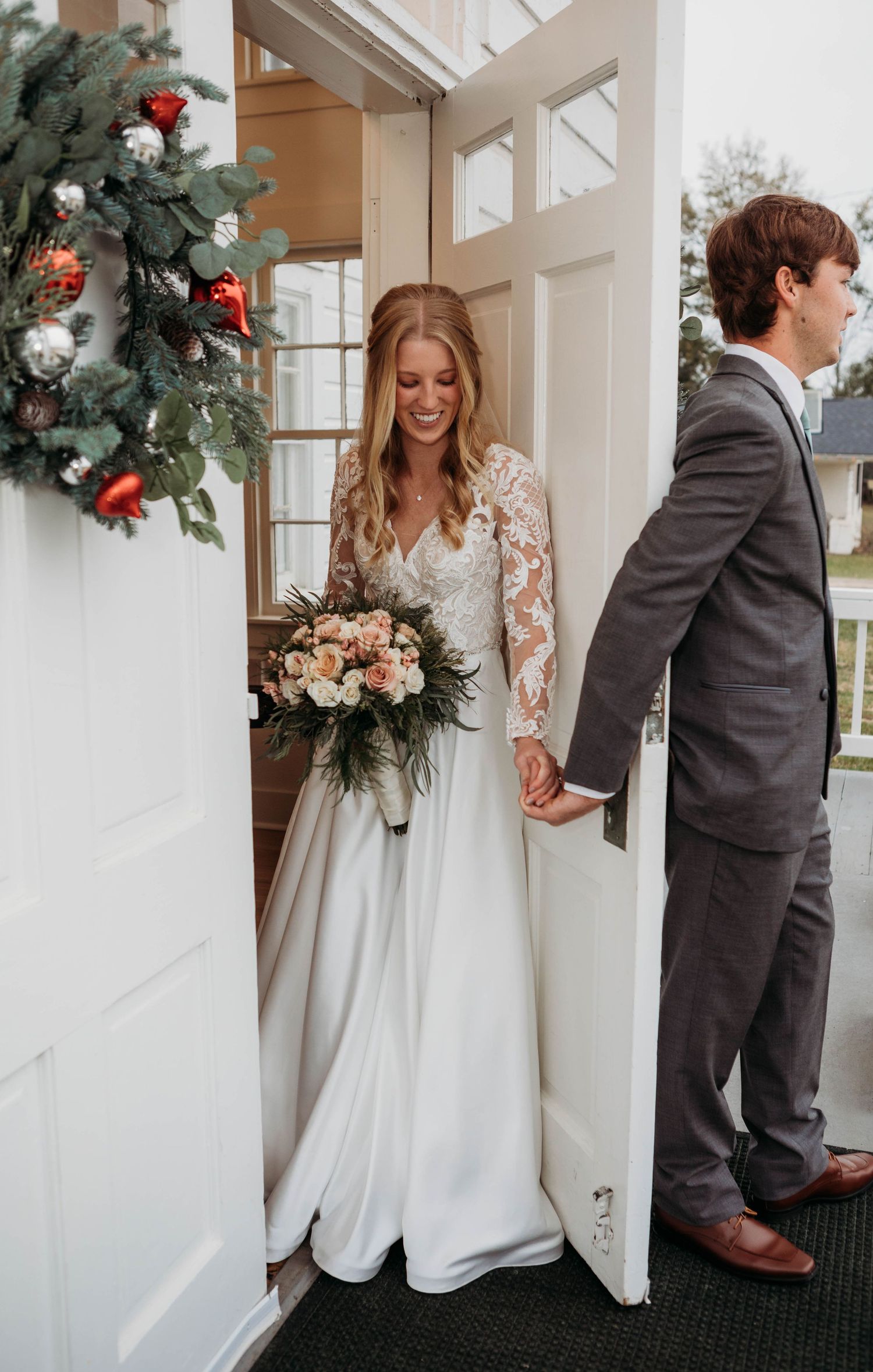 First look between newlyweds at doorway decorated with holiday wreath and florals.