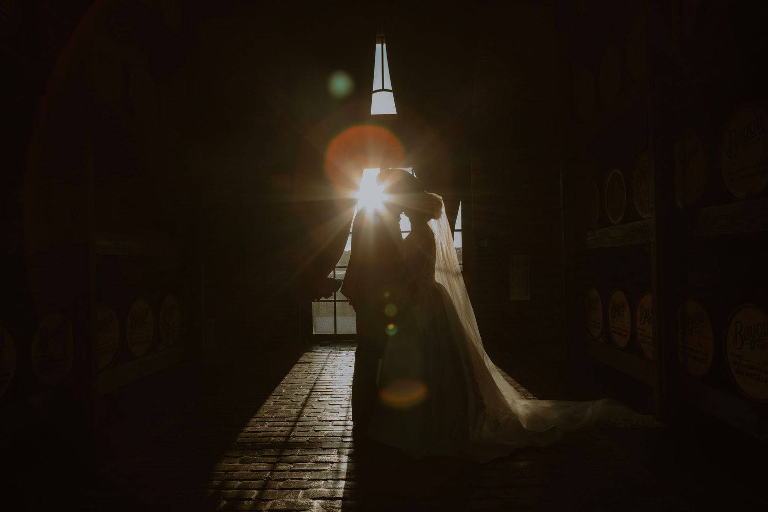 Silhouetted bride and groom share a romantic moment in a dark archway with golden sunlight glowing behind them.