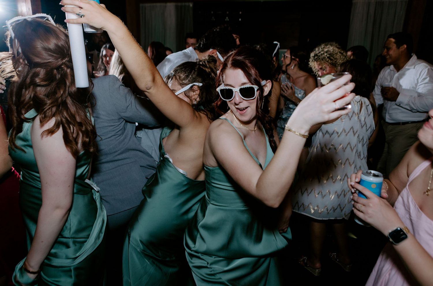 Women in green satin bridesmaid dresses dancing at a wedding reception party.
