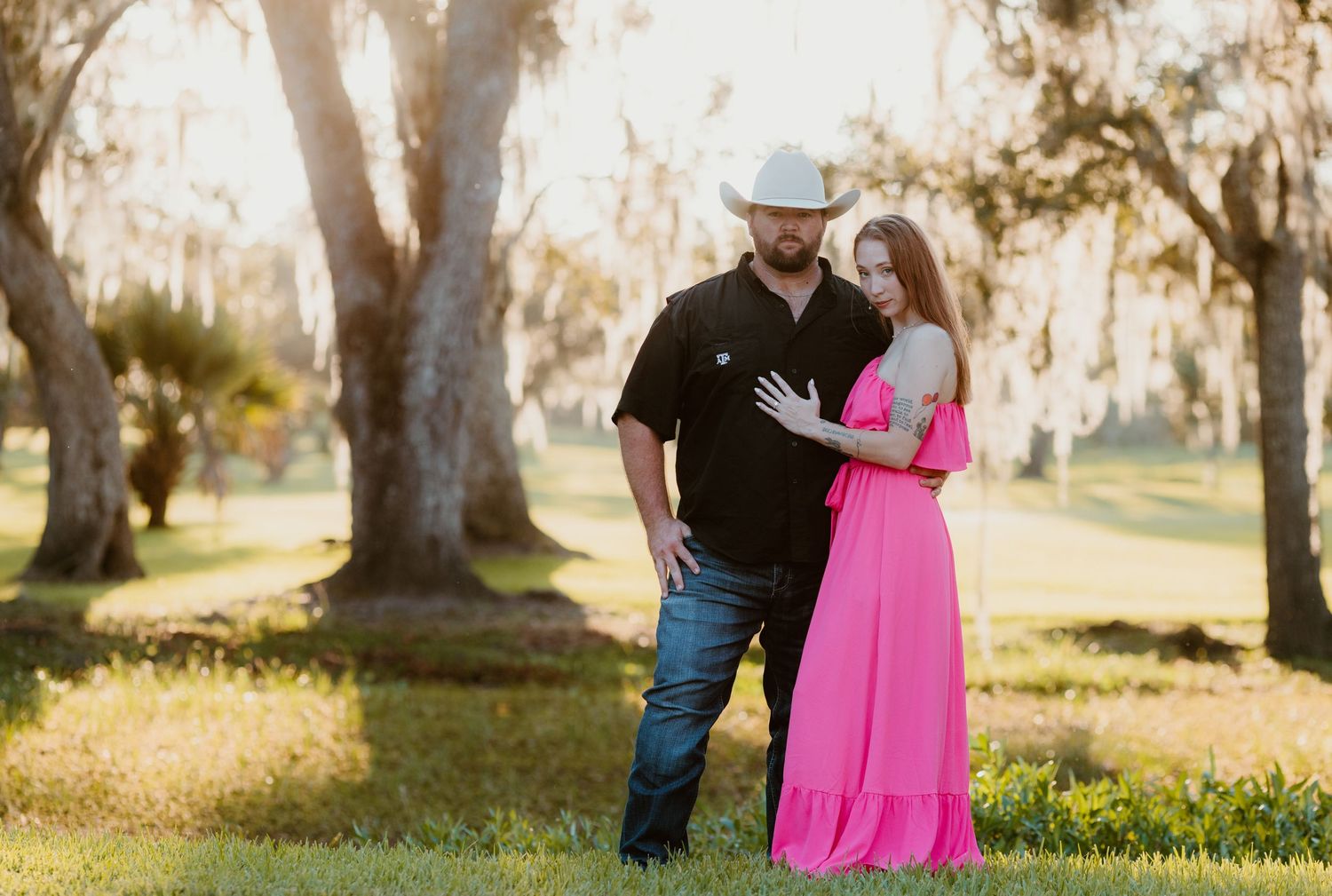A couple embraces in a sun-drenched park with tall trees creating a romantic autumn atmosphere.