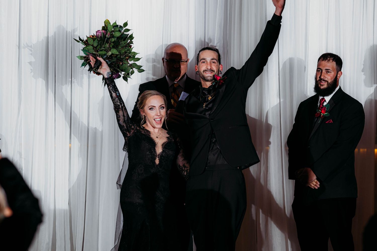 Newlywed couple celebrating with raised hands and bouquet at their joyful wedding ceremony.