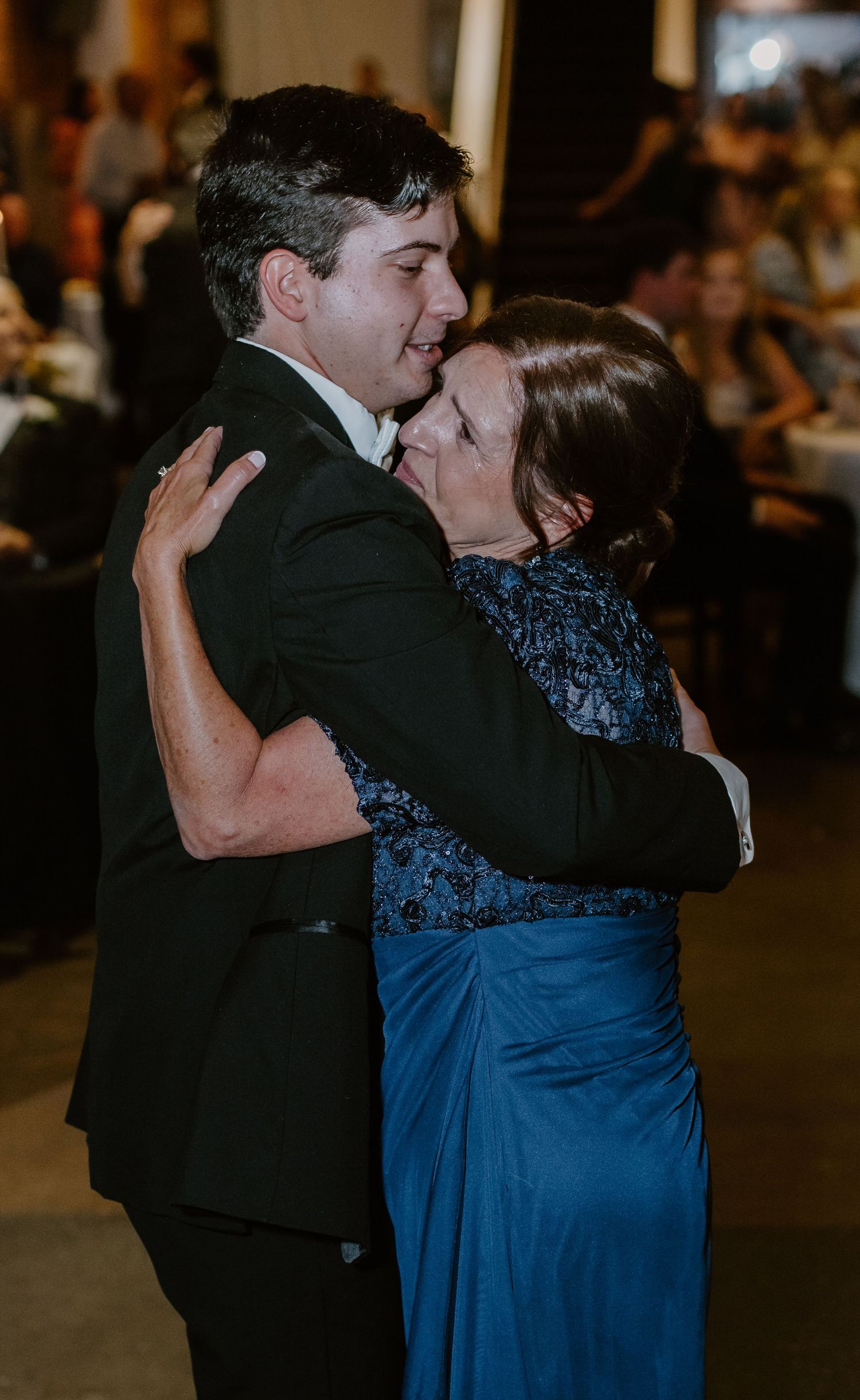 A young man in a tuxedo shares a tender mother-son dance at a wedding reception.