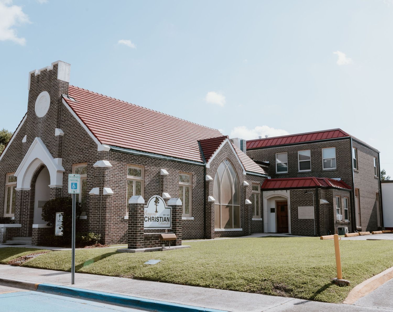 Historic brick church building with red tile roof and modern annex under blue sky.