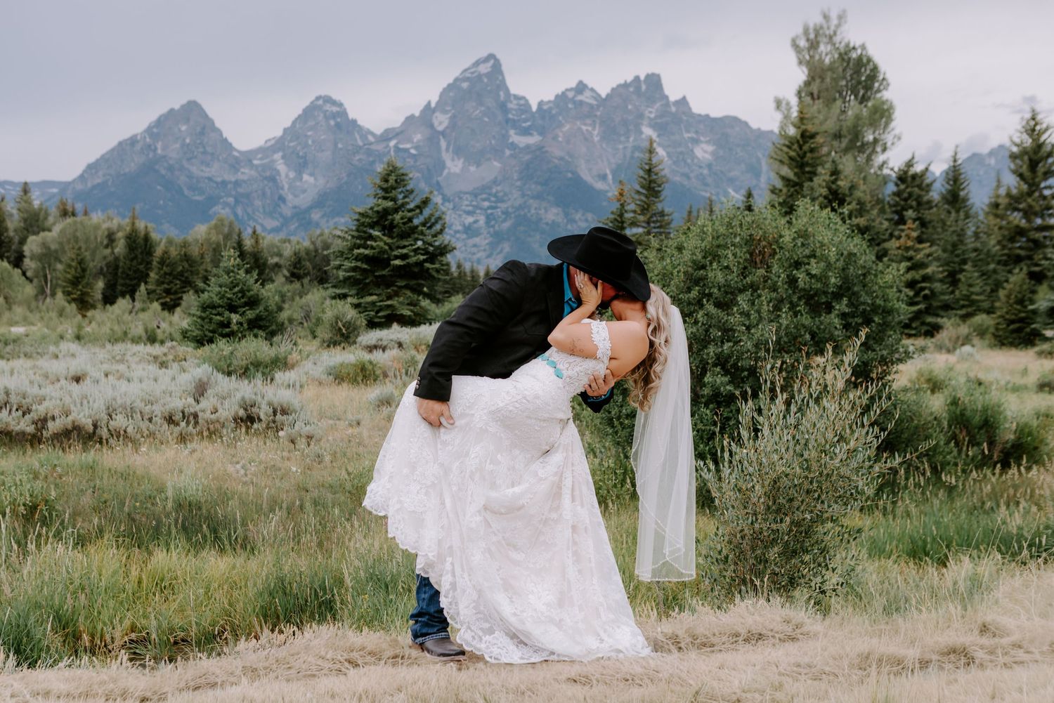 Couple sharing a romantic dip kiss in wedding attire with Grand Teton mountains backdrop in Wyoming.