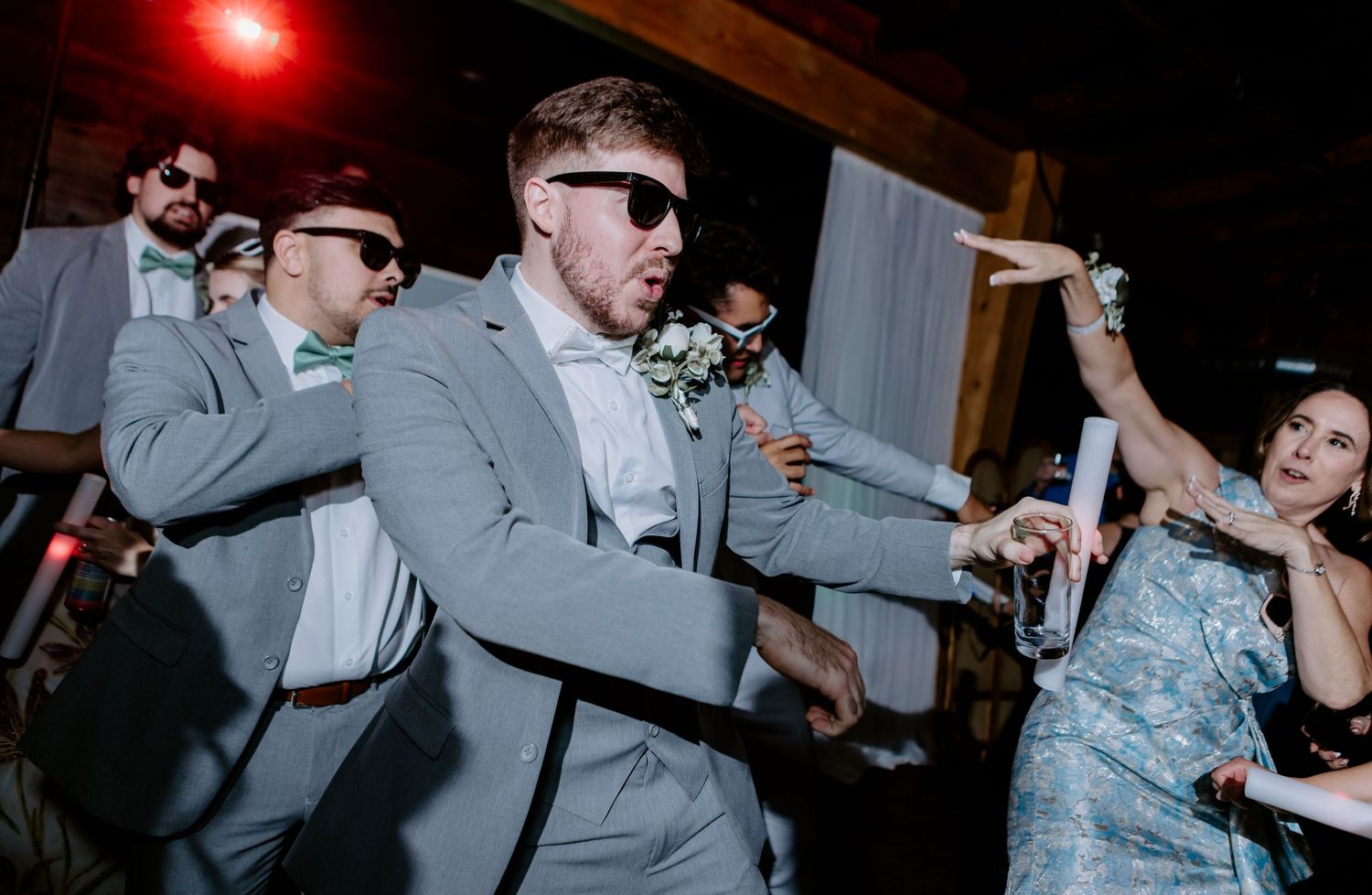 Groom and groomsmen wearing sunglasses dance energetically on the wedding reception dance floor.