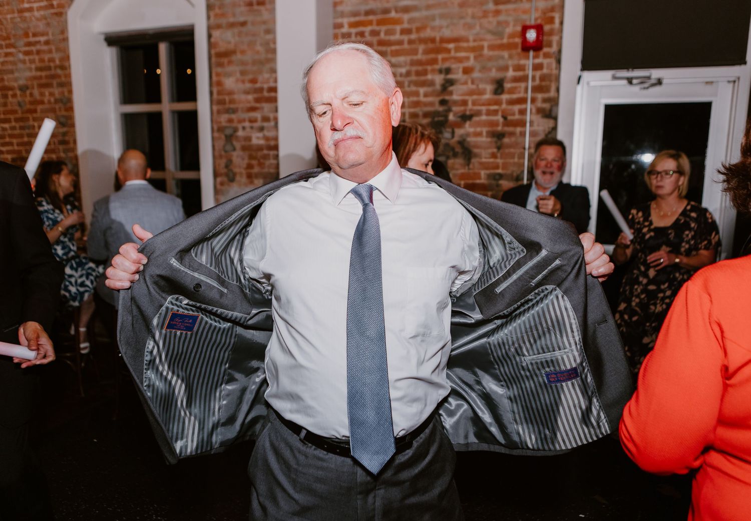 Older gentleman proudly opens his suit jacket while dancing at a wedding reception celebration.