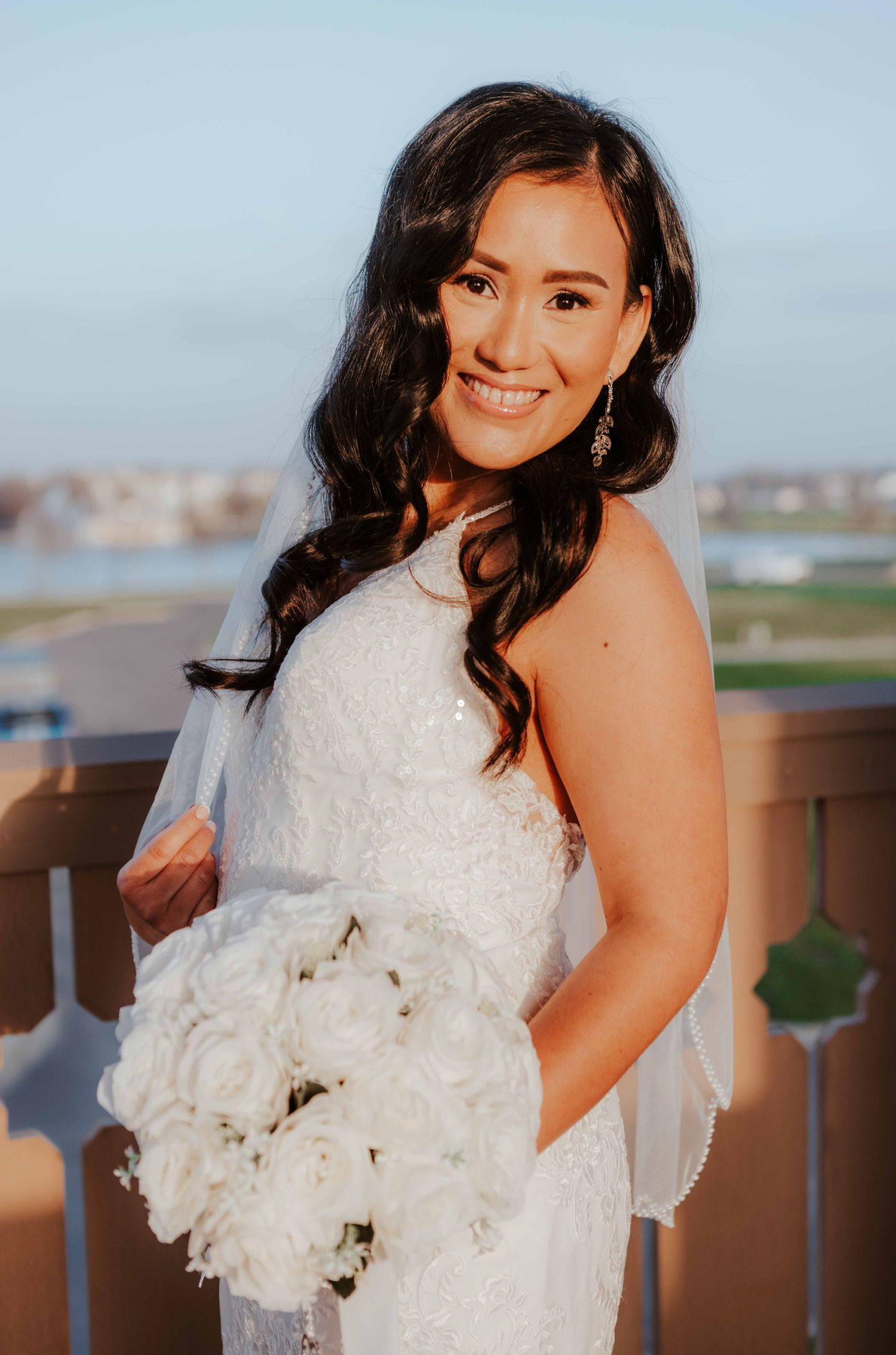 A bride in a white strapless lace wedding dress poses with her bouquet of white peonies on an outdoor balcony.