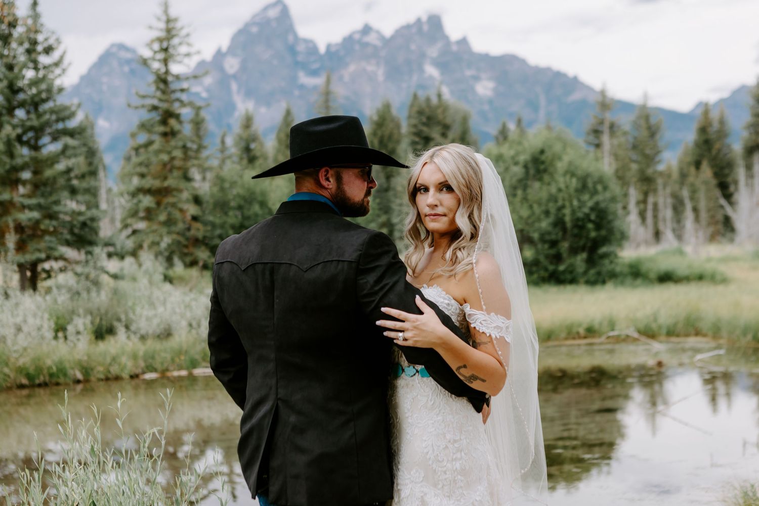Bride and groom share a romantic moment by a mountain lake in Grand Teton National Park, with scenic peaks in the background.