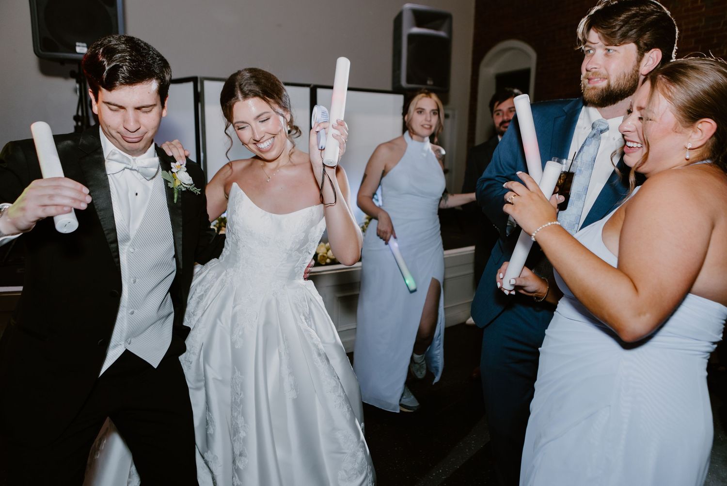 Bride and groom dancing with wedding guests holding light-up batons at a lively wedding reception.