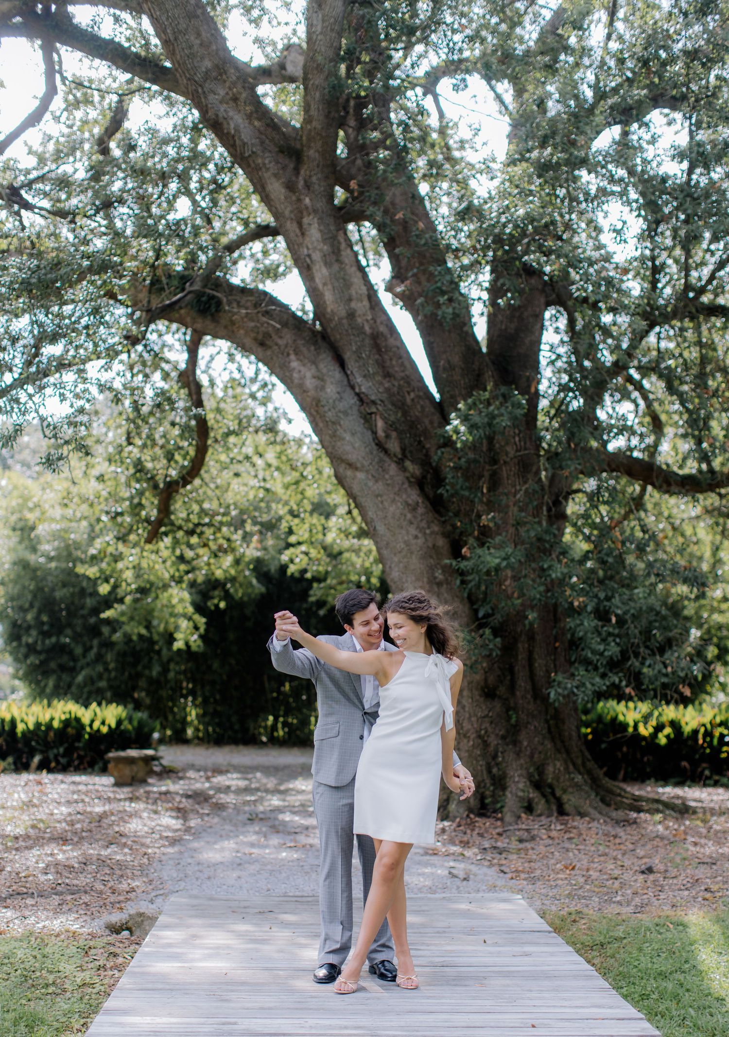 A romantic dance sequence unfolds on a wooden boardwalk beneath a majestic oak tree in a natural outdoor setting.