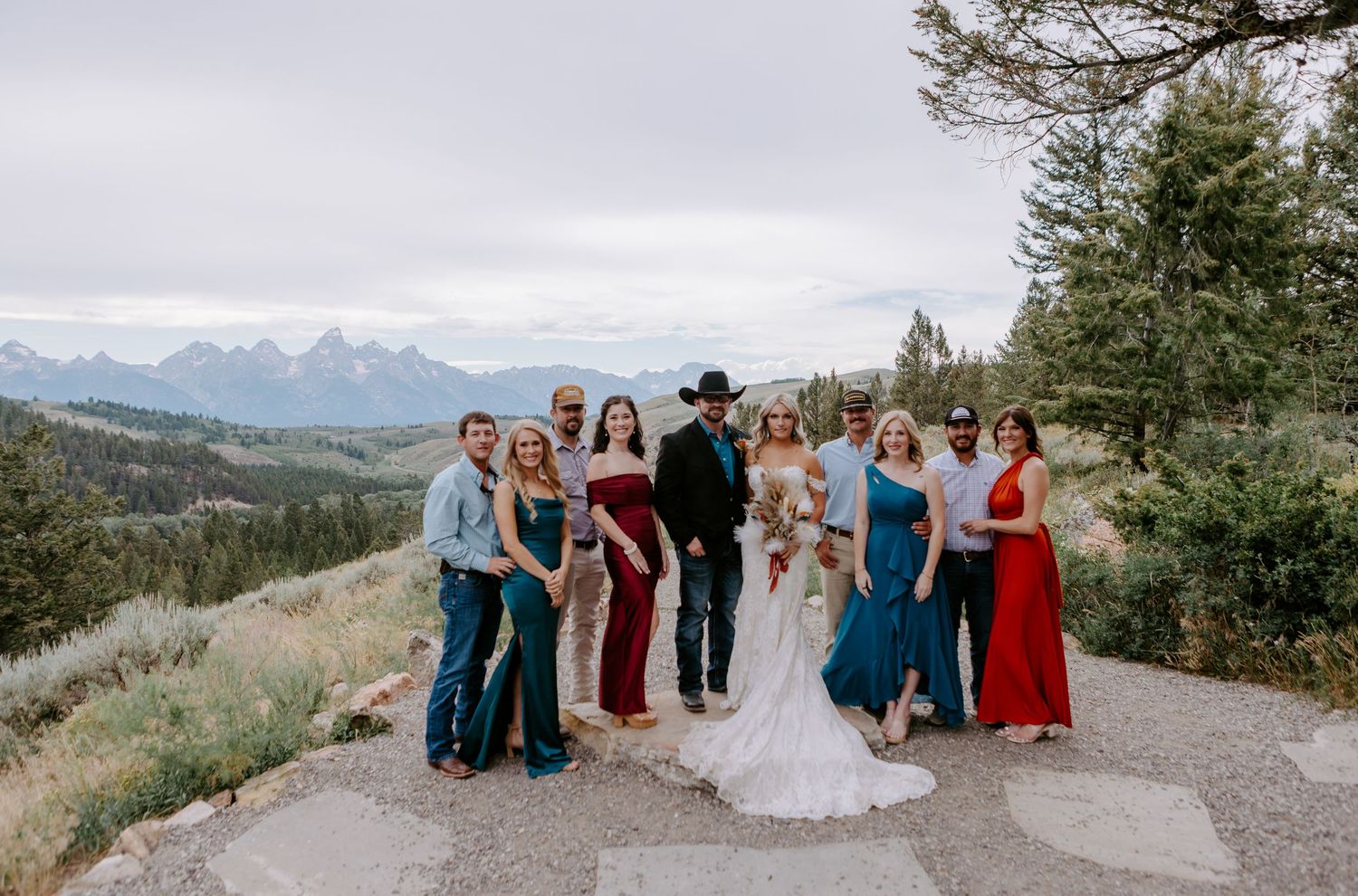 Wedding party posing outdoors with stunning mountain and valley views in background on a cloudy day.